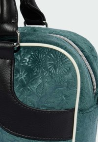 Sac à main avec un design floral en relief teal, des accents en cuir noir, une fermeture éclair argentée et des détails en piping blanc créant une apparence texturée.