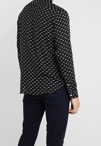 Camisa negra de botones con un diseño de estampado de animales en blanco repetido, con mangas largas y un dobladillo curvado. Confeccionada en tejido ligero.