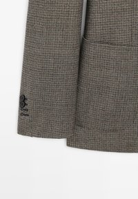 Brown houndstooth patterned blazer featuring a single breast pocket, two-button cuff, and textured fabric for a tailored look.