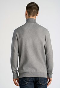 Grau gestrickter Pullover mit hohem Kragen, gerippten Bündchen und Saum. Der Stoff hat eine glatte Textur und wird mit dunkelblauen Jeans kombiniert.