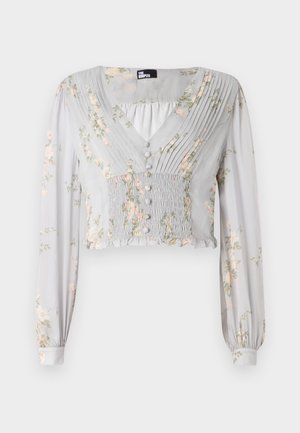 Light grey cropped blouse featuring floral patterns, pleated front, v-neck, button details, and long sleeves with ruffled cuffs.