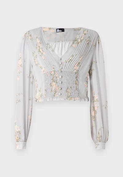 Blouse courte gris clair avec motifs floraux, devant plissé, décolleté en V, détails de boutons, et manches longues avec poignets froncés.