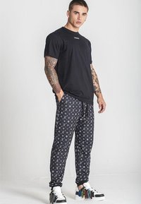 Crna majica kratkih rukava u paru s uzorcima crnih trenirki koje imaju bijele logotipe, nosi se s šarenim tenisicama. Opušteni outfit.