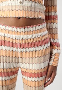 Csíkos kötött otthoni viselet szett, jellegzetes zig-zag mintával narancssárga, krémszínű és barna árnyalatokban; testhezálló crop top és magas derekú nadrág.