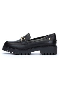 Mocasines de cuero negro con un acento de hebilla dorada, suela gruesa y estriada, textura suave y diseño de tacón plano.