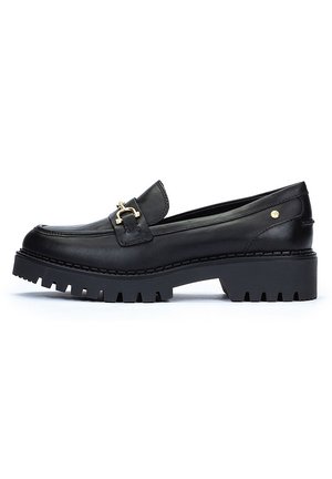 Mocasines de cuero negro con un acento de hebilla dorada, suela gruesa y estriada, textura suave y diseño de tacón plano.