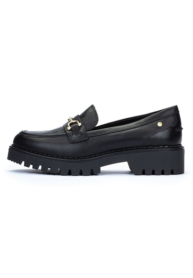Mocasines de cuero negro con un acento de hebilla dorada, suela gruesa y estriada, textura suave y diseño de tacón plano.
