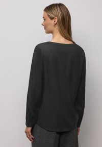 Blusa nera a maniche lunghe con vestibilità rilassata, texture liscia e scollatura ampia, abbinata a pantaloni a quadri fantasia.