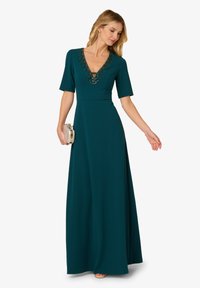 Dlouhé smaragdově zelené šaty s výstřihem do V, krátkými rukávy a zdobením korálky kolem výstřihu. Volný střih s bočním rozparkem.
