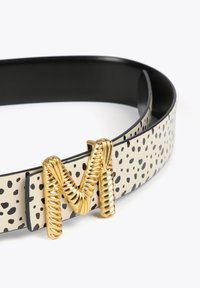 Ceinture avec un design crème et noir à pois, dotée d'une boucle en or en forme de 'M' torsadée. Texture en cuir lisse avec une finition brillante.