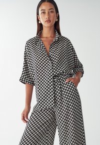 Black and white patterned shirt and pants set, featuring a collared shirt with short sleeves and a loose fit, with a geometric design.