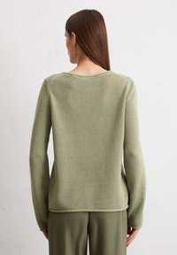Maglione verde lavorato a maglia con finitura texturizzata, maniche lunghe e scollatura rotonda, abbinato a pantaloni verdi coordinati.