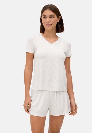 Mujer con camiseta de manga corta V cuello en gris claro con ribete de encaje y pantalones cortos a juego, de pie contra un fondo liso y claro.