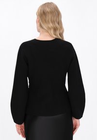 Tricou negru cu mânecă lungă, cu decolteu rotund și o siluetă ajustată, realizat dintr-un material moale și neted, cu o textură subtilă pe mâneci.