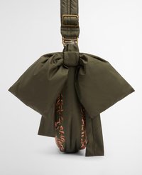 Olivgrüne Tasche mit einem großen Schleifendetail, aus weichem Stoff gefertigt. Verfügt über einen gemusterten Gurt in contrasting Farben und goldfarbene Hardware.