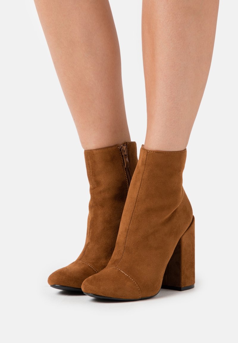 Bottines en daim marron avec un bout pointu et un talon bloc. Dotées d'une fermeture éclair à l'arrière et d'une texture lisse.
