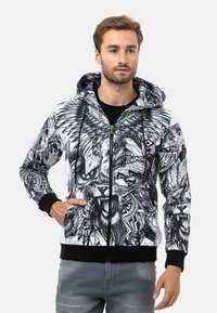 Kapuzensweatshirt mit Reißverschluss, das schwarz-weiße Grafikdrucke von Löwen und tribal Muster zeigt. Hergestellt aus weichem Stoff mit gerippten Bündchen.