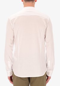 Camicia bianca a maniche lunghe con orlo curvo, polsini bottonati e una texture liscia. Presenta un design con yoke sul retro per garantire struttura.