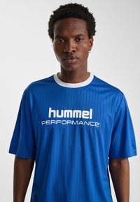 Blå sporttröja med randig textur, korta ärmar och vit krage. Har "hummel PERFORMANCE"-logotyp i vitt på framsidan.