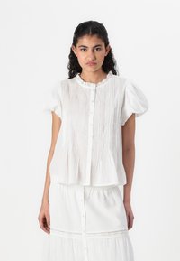 Hvit kortermet bluse med knapper foran, blondekrage, plissédetaljer og flared søm. Stoffet ser lett og teksturert ut.