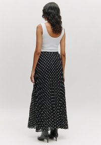 Zwarte plissé rok met witte stippen, gedragen met een witte tanktop, gecombineerd met zwarte hoge laarzen. Focus op de textuur van de stof en het patroon.