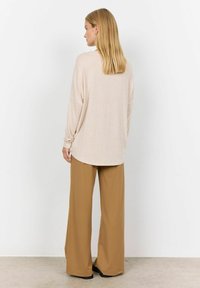 Beige long-sleeve top with a relaxed fit and rounded hem, paired with tan wide-leg trousers; smooth texture and minimal detailing.
