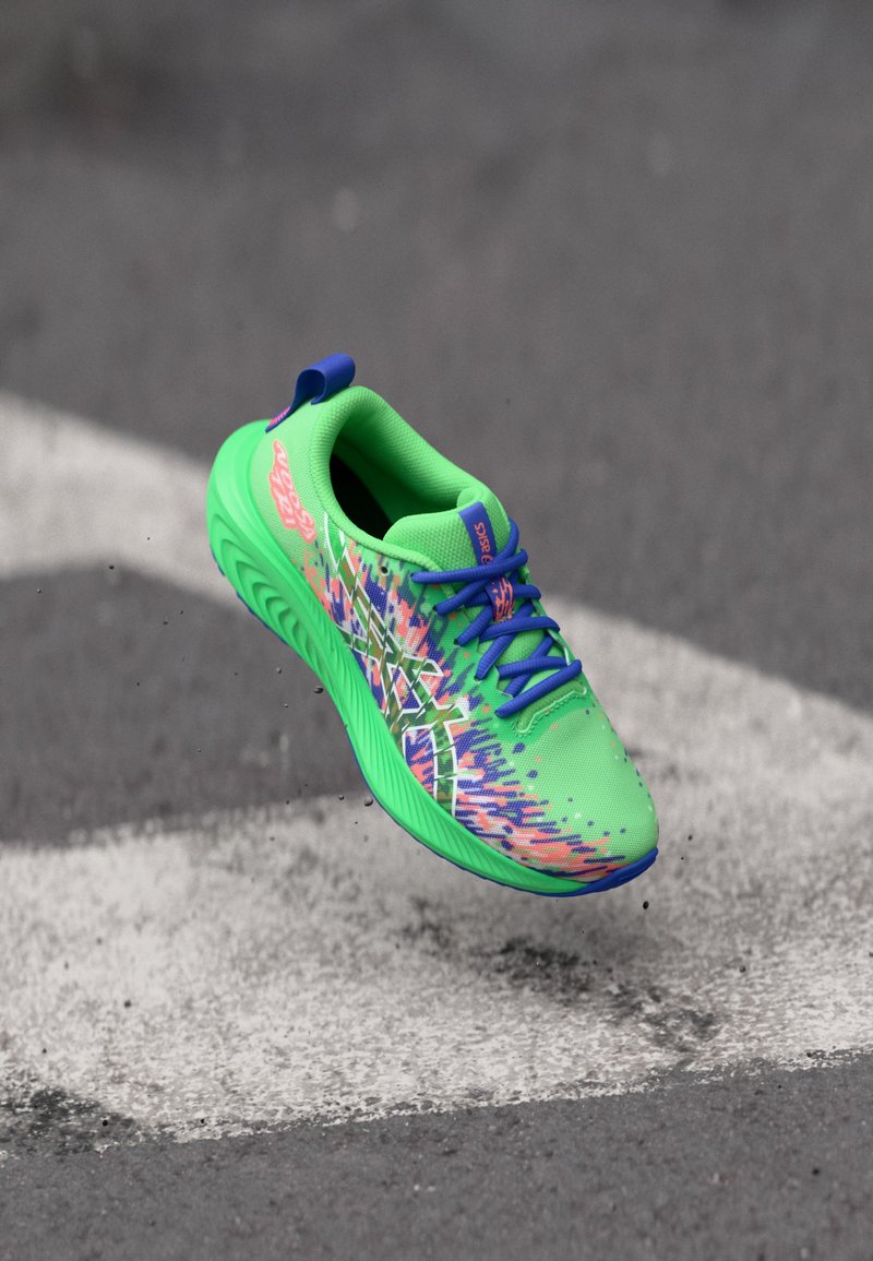 Zapatilla deportiva verde brillante con una parte superior de malla texturizada y patrones multicolores vibrantes, cordones azules y una suela acolchada.