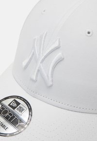 Boné de beisebol branco com um logotipo bordado branco dos New York Yankees, apresentando uma textura de tecido suave e uma aba curvada.