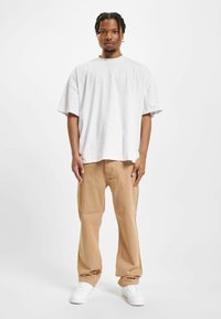 Camiseta de algodón blanca de corte extragrande combinada con pantalones rectos beige y zapatillas blancas. El conjunto presenta un ajuste relajado y un diseño sencillo.