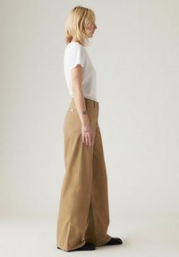 Wijdvallende, kaki broek met een hoge taille, gemaakt van stevig materiaal, gecombineerd met een fitted witte t-shirt. Strakke lijnen en geen zichtbare patronen.
