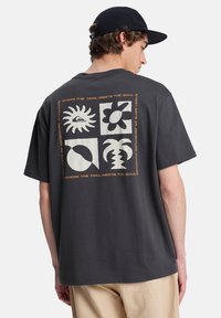 Σκούρο γκρι βαμβακερό t-shirt με γραφικό σχέδιο στο πίσω μέρος που περιλαμβάνει τέσσερα τετράγωνα με σχέδια και κείμενο, σε άνετη γραμμή.