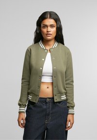 Olive zelena bomber jakna s srebrnimi gumbi, rebrastim ovratnikom in zapestji ter belimi črtami. Mehka tkanina in prilega oblikovanju.