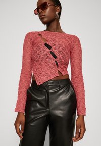 Rosa blonder langermet topp med en utskjæringsdesign, kombinert med svarte skinnbukser. Toppen har et teksturert mønster.