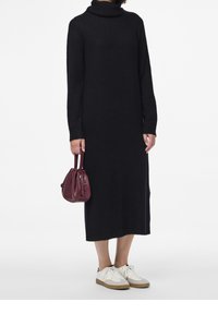Vestito a maglia nero a collo alto, in una vestibilità rilassata, di lunghezza fino al ginocchio. Abbinato a una piccola borsa bordeaux e scarpe da ginnastica bianche.