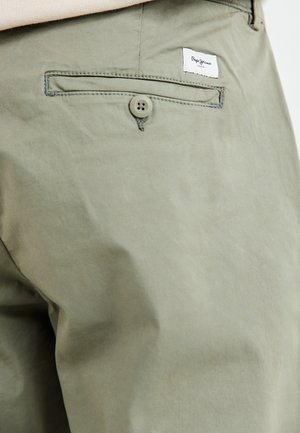 Kerged oliivrohelised puuvillased püksid, millel on tagatasku, nööbijooks ja väike brändi silt õmmeldud tasku kohale.