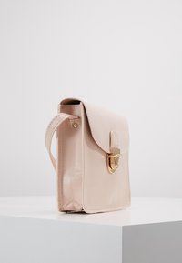 Borsa in pelle rosa pallido con chiusura a patta e clasp dorato, poggiata su una superficie bianca con sfondo semplice.
