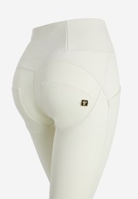 Leggings bianchi a vita alta realizzati in tessuto elastico, con cuciture decorative e un piccolo logo nero e oro sulla tasca posteriore.
