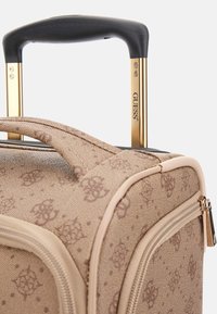 Valigia rigida beige con manico retrattile dorato, tessuto testurizzato, motivo a logo marrone e dettagli beige, dotata di chiusura con zip.