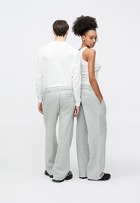 Pilkos laisvo stiliaus sportinės kelnės su elastine juosmens juosta, derinamos su balta ilgomis rankovėmis palaidine ir baltu berankoviu viršutiniu drabužiu.