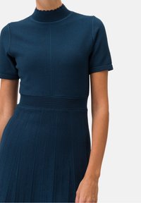 Stickad klänning i mörkblått med en scalloped hög halsringning, korta ärmar, texturerad liv med plisserad kjoldesign.