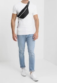 Svart crossbody-väska med en mjuk yta, justerbar rem och dragkedjestängning. Bärs över en vit t-shirt och ljusblå jeans.