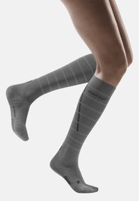 Calze a compressione grigie con design a coste, caratterizzate da strisce orizzontali e marchio nero. Texture liscia; lunghezza fino al ginocchio.