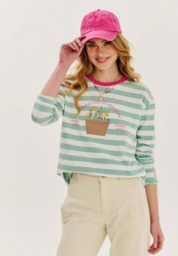 Zeleno-mentolovo a biele pruhované košeľové tričko s dlhým rukávom a grafikou kvetinového koša; ružová čiapka; krémové nohavice. Text zahŕňa "Kôš plný slnečníc."