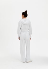 Felpa bianca con cappuccio e cordini, abbinata a pantaloni tuta larghi e coordinati. Entrambi hanno tasche anteriori e una consistenza morbida.