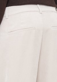 Pantalons en velours côtelé beige avec des côtes verticales, une coupe droite et deux poches arrière avec de subtils détails de couture.
