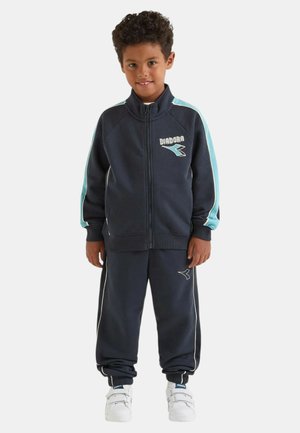 Tuta da bambino blu navy in tessuto morbido con dettagli azzurri. Comprende giacca con zip e pantaloni con polsini elastici, con logo sul petto e sulla gamba.