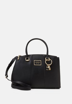 Sac à main Guess noir avec doubles poignées, bandoulière amovible, plaque logo dorée et porte-clés avec détail de serrure sur fond blanc.
