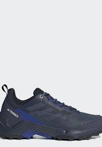 Tmavomodrá turistická topánka Adidas Terrex s čiernou podrážkou, sieťovaným zvrškom a modrými akcentmi, zobrazená zvonku.