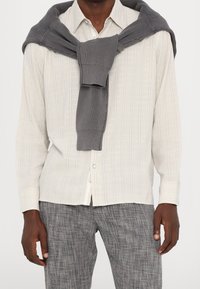 Light gray striped button-up shirt, gray knit sweater tied around neck, gray textured pants. Cotton blend material with a casual fit.