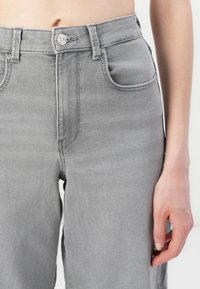 Grijze denim jeans met een hoge taille, vijf-pocket ontwerp en metalen knoopsluiting. De textuur is glad met subtiele stikdetails.